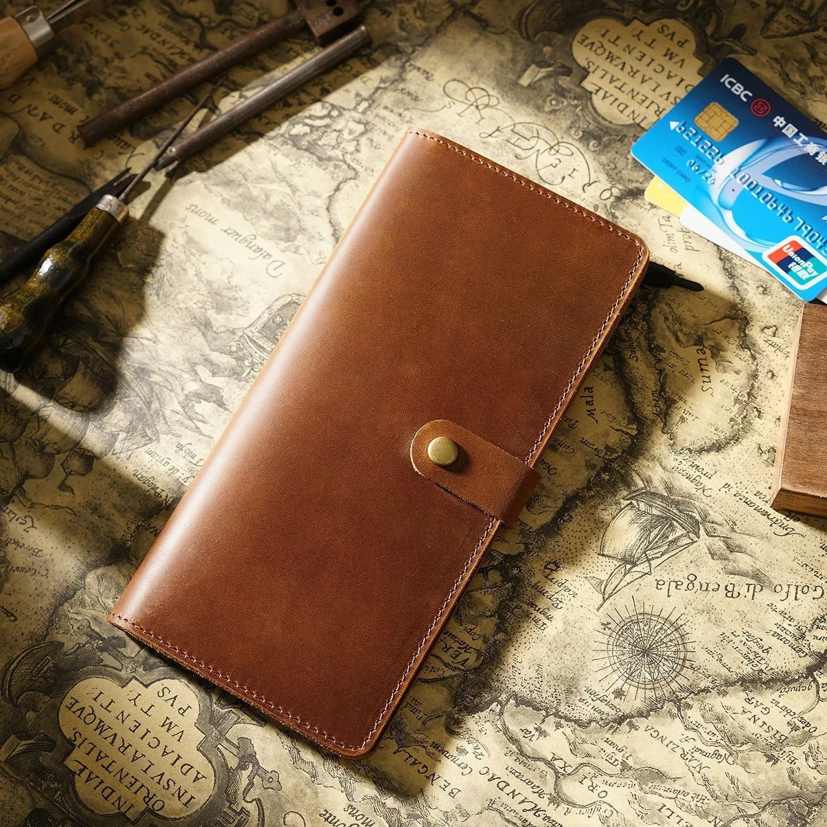 A brown genuine leather long bi-fold wallet with a snap closure resting on aged paper.