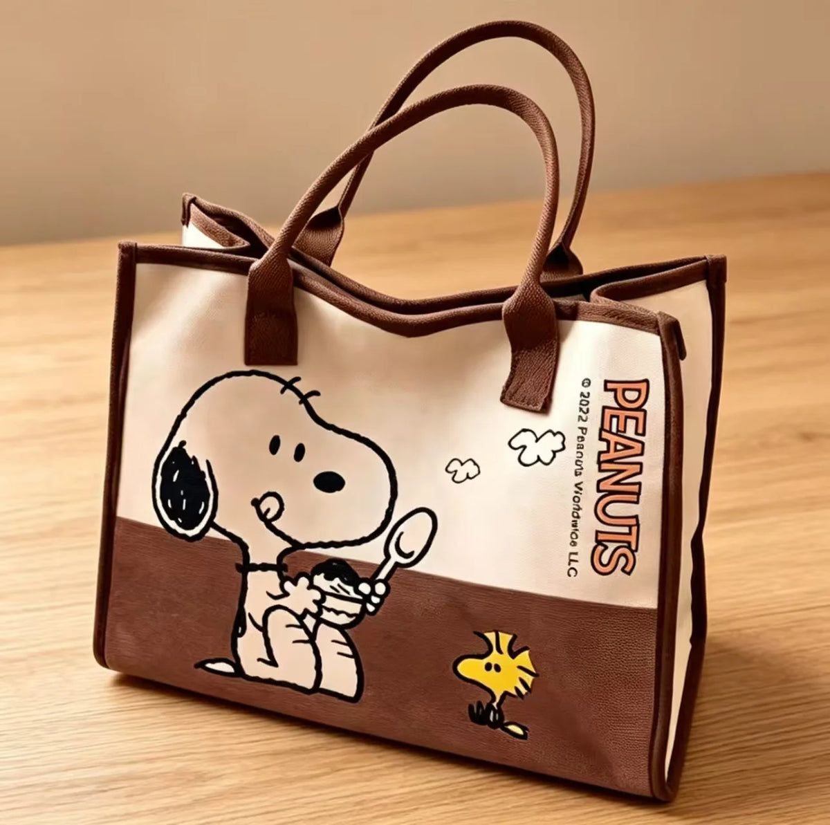 A brown canvas shoulder bag featuring a Snoopy cartoon design on the front.