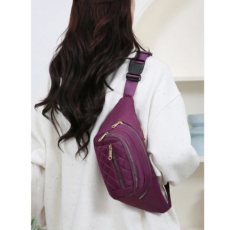 A purple nylon crossbody belt bag worn by a woman with long dark hair, shown from the back.