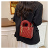 A woman holds a red quilted diamond grid textured crossbody bag against a black blazer.