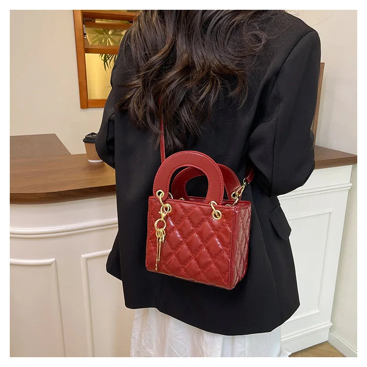 A woman holds a red quilted diamond grid textured crossbody bag against a black blazer.