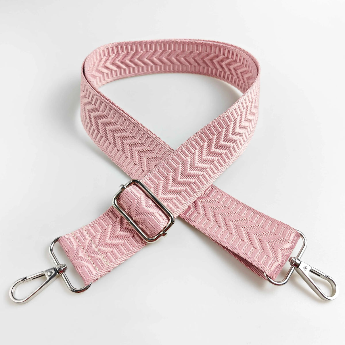 A pink woven handbag strap with an arrow jacquard pattern shown crossed on a white background.