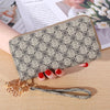 Cartera con cremallera de cuero sintético beige y patrón geométrico negro, apoyada sobre una superficie de madera.
