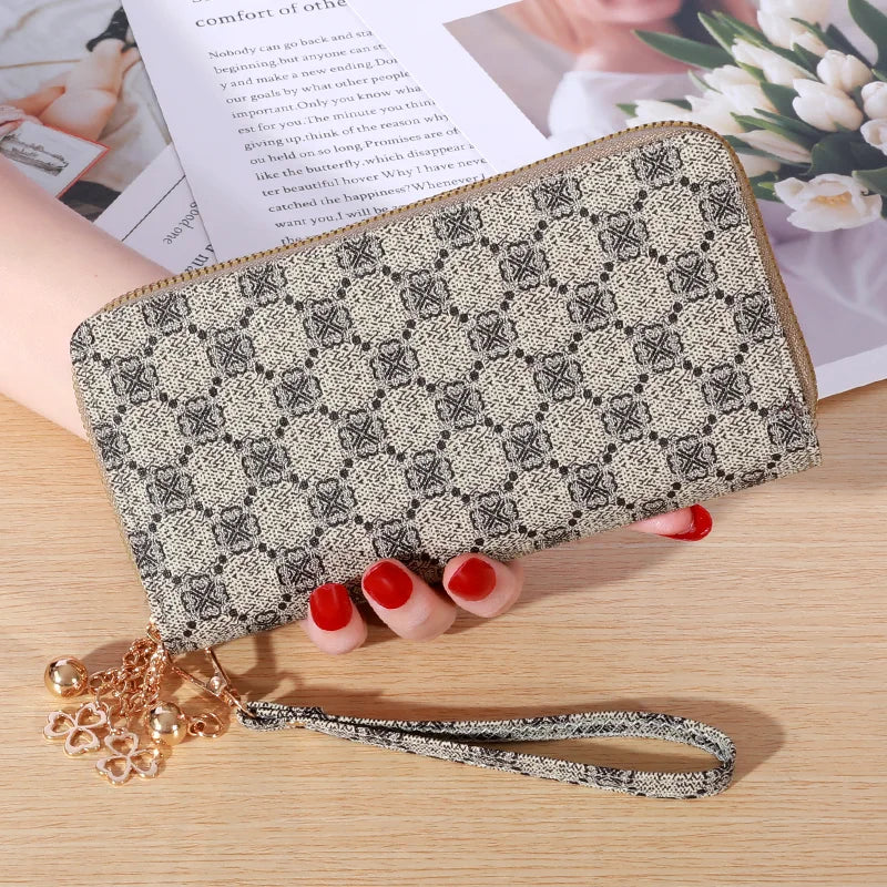Cartera con cremallera de cuero sintético beige y patrón geométrico negro, apoyada sobre una superficie de madera.
