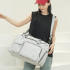 A woman holds a light gray quilted portable travel duffle bag against a white background.