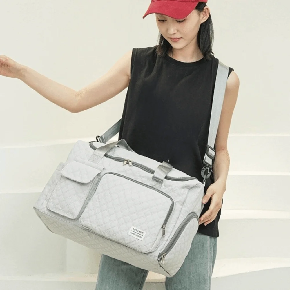 A woman holds a light gray quilted portable travel duffle bag against a white background.