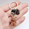 A small brown teddy bear pendant keychain with a coffee cup charm and silver ring attached.