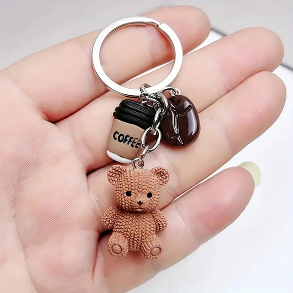 A small brown teddy bear pendant keychain with a coffee cup charm and silver ring attached.