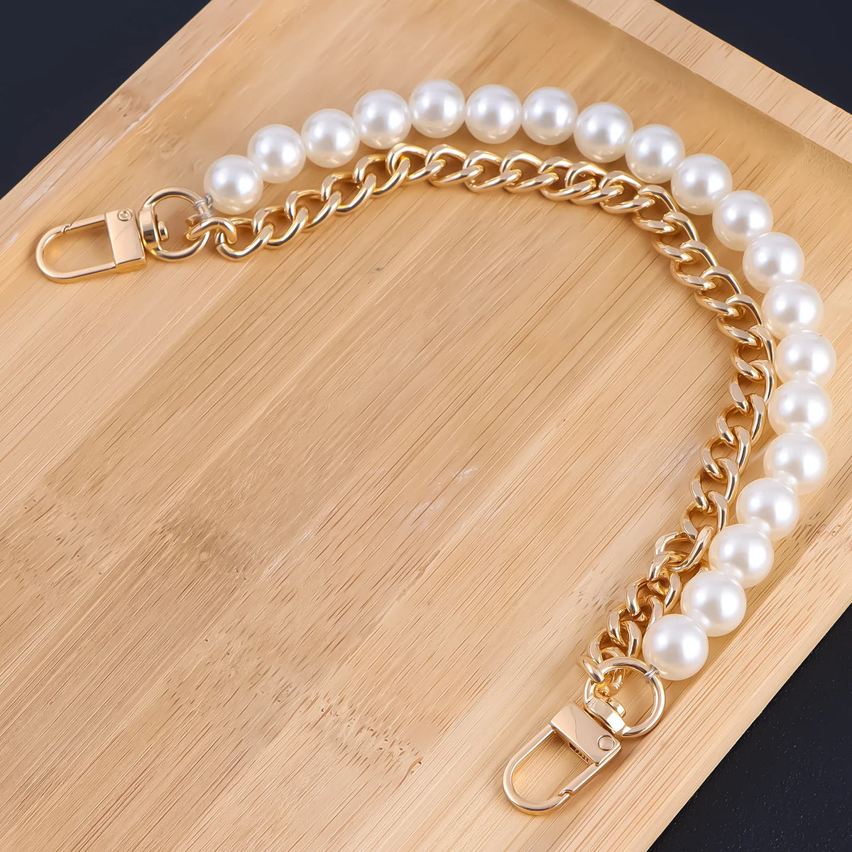 A gold chain necklace with a pearl strand is laid on a wooden cutting board.