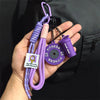 A purple nylon fitness keychain with a yellow dumbbell charm is held in a hand against a black background.