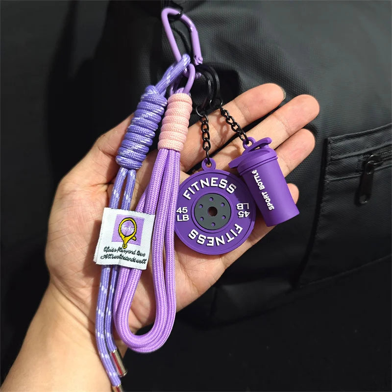 A purple nylon fitness keychain with a yellow dumbbell charm is held in a hand against a black background.