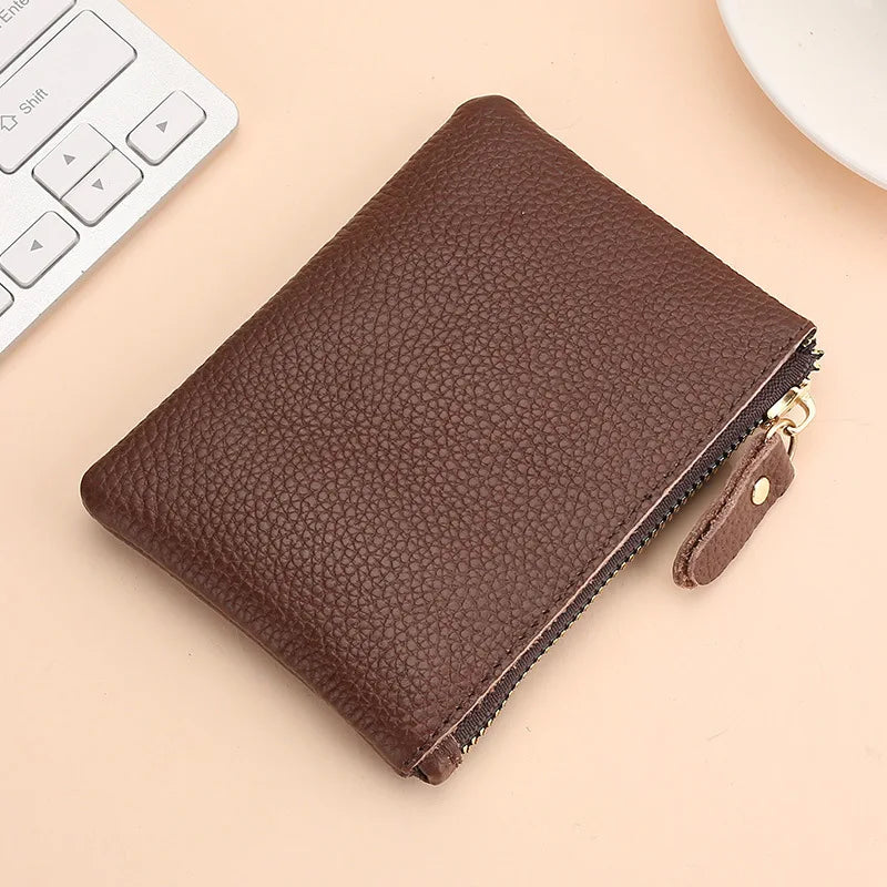 A brown genuine leather mini zipper coin and card purse resting on a light beige surface next to a white computer keyboard.