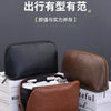 A brown leather multi-layer cable organizer pouch is displayed next to a black version on a stack of white books.