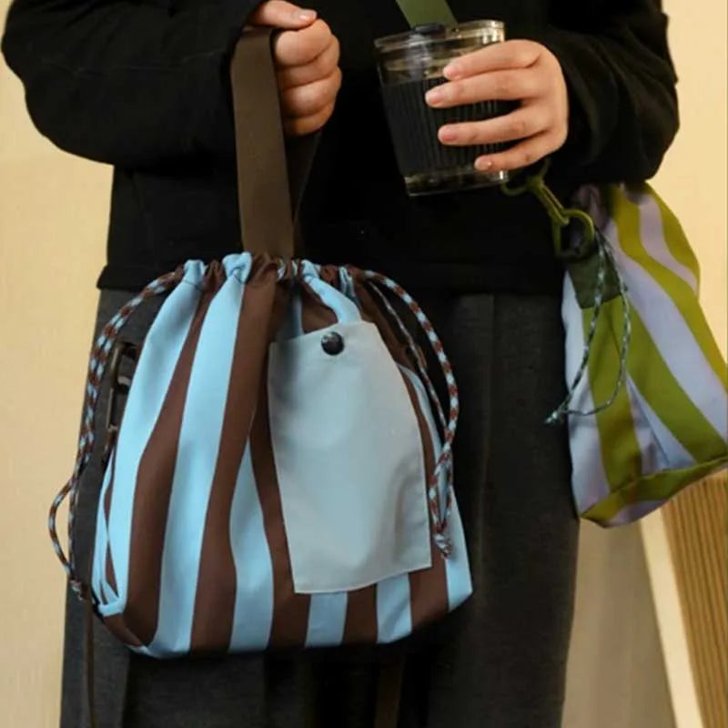 A person holds an insulated lunch bag with a striped design in shades of blue and brown.