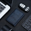 A dark blue magnetic leather card wallet resting on a black surface next to a laptop and a stylus.