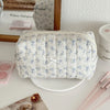 A white quilted cosmetic bag with a light blue floral pattern rests on a white surface.