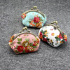Two vintage rose print canvas coin purses, one light blue and one pink, resting on a gray textured surface.