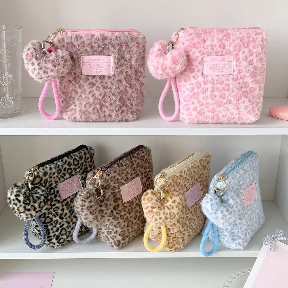Pink leopard print makeup bags with fuzzy appliqués and pink straps displayed on a white shelf.