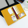 A yellow PU leather passport holder with a dark red accent and white pen slots is displayed on a black case.