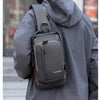 A man wearing a gray hoodie carries a dark gray anti-theft zippered crossbody bag.