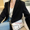A woman models a black blazer and white top, holding a white quilted handbag with a gold chain strap.