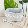 Light blue fabric storage basket with white lace trim and small bows sitting on a book.