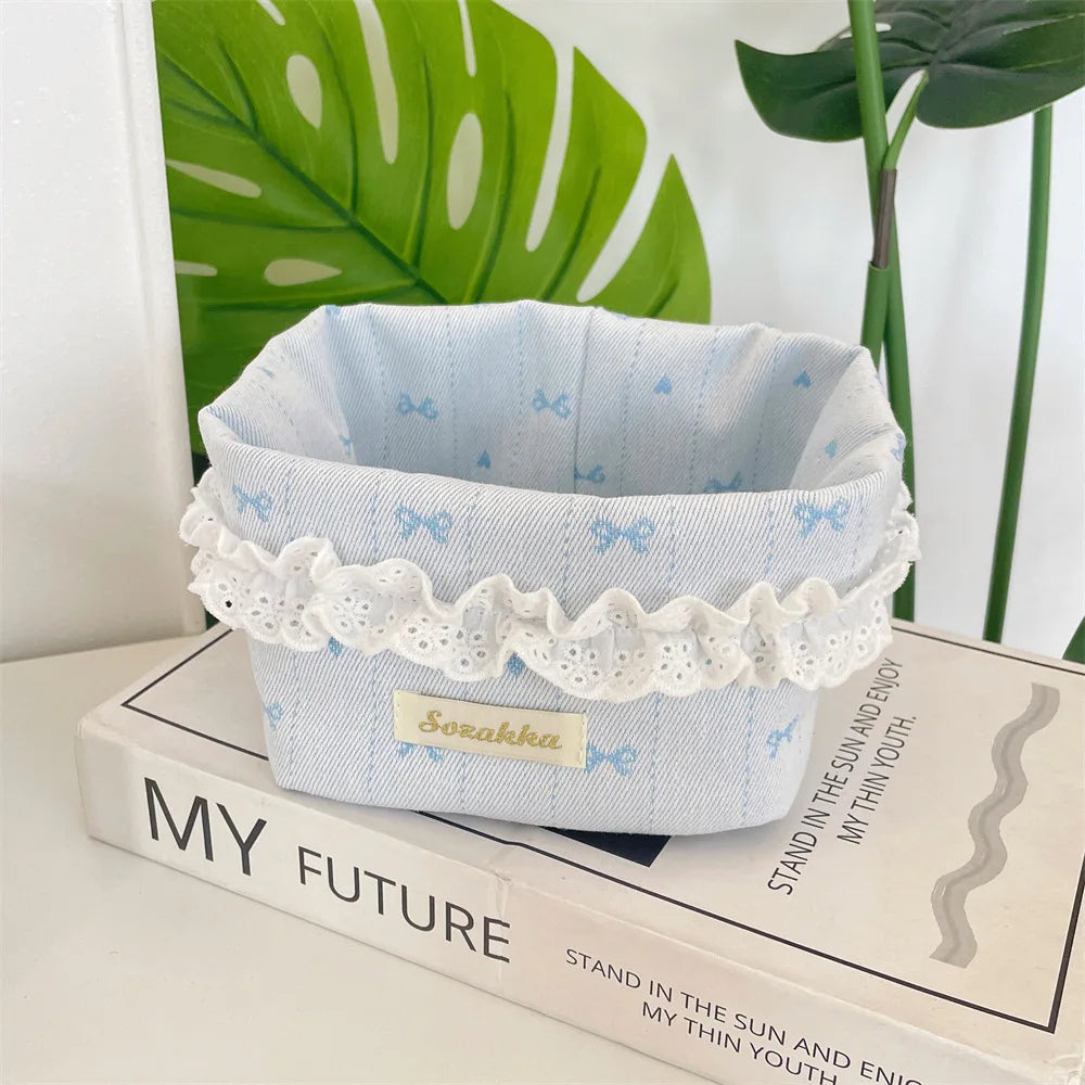 Light blue fabric storage basket with white lace trim and small bows sitting on a book.