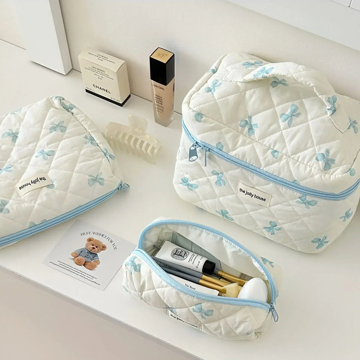Sac de rangement cosmétique rembourré blanc avec motif nœud et bordure bleu clair, à côté d'une pochette assortie et d'un pin