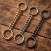 Three metal chain extenders or clasps in gold and black finishes laid on a wooden surface.