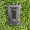 A dark gray slim aluminum metal ID card wallet lying on green grass.