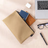 A tan multi-functional organizer tool kit bag next to a blue notebook and a brown leather item on a light surface.