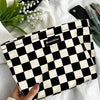 A black and white checkered cosmetic storage bag resting on a white towel with green leaves.