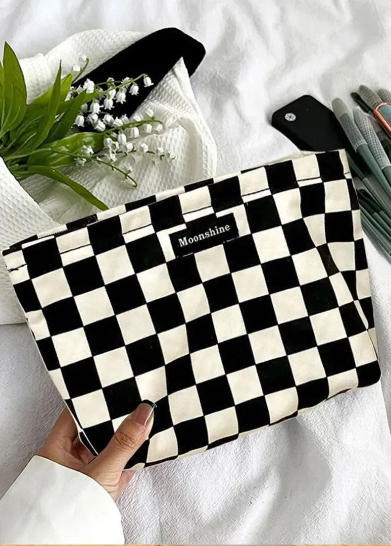 A black and white checkered cosmetic storage bag resting on a white towel with green leaves.