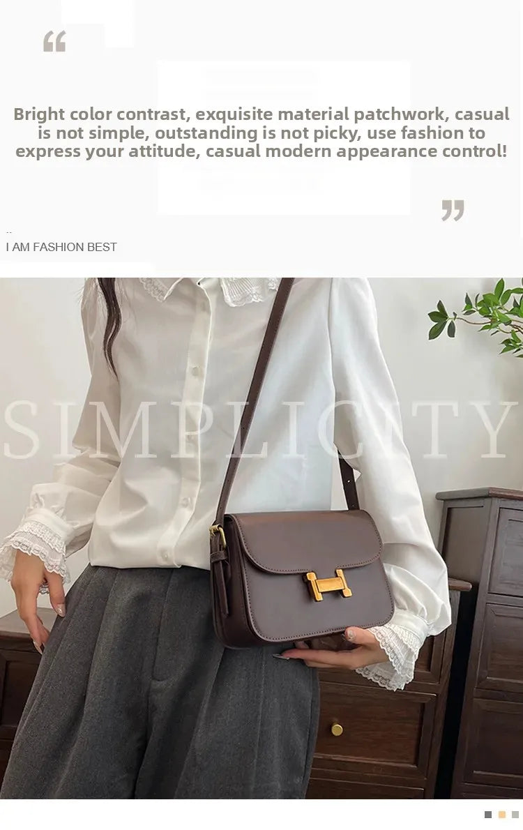 Eine Frau präsentiert eine braune Leder-Ein-Schultertasche mit goldener Schnalle vor weißem Hemd und grauem Rock.