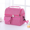 A pink reusable insulated lunch bag with a zippered compartment and a separate pocket is shown on a white surface.