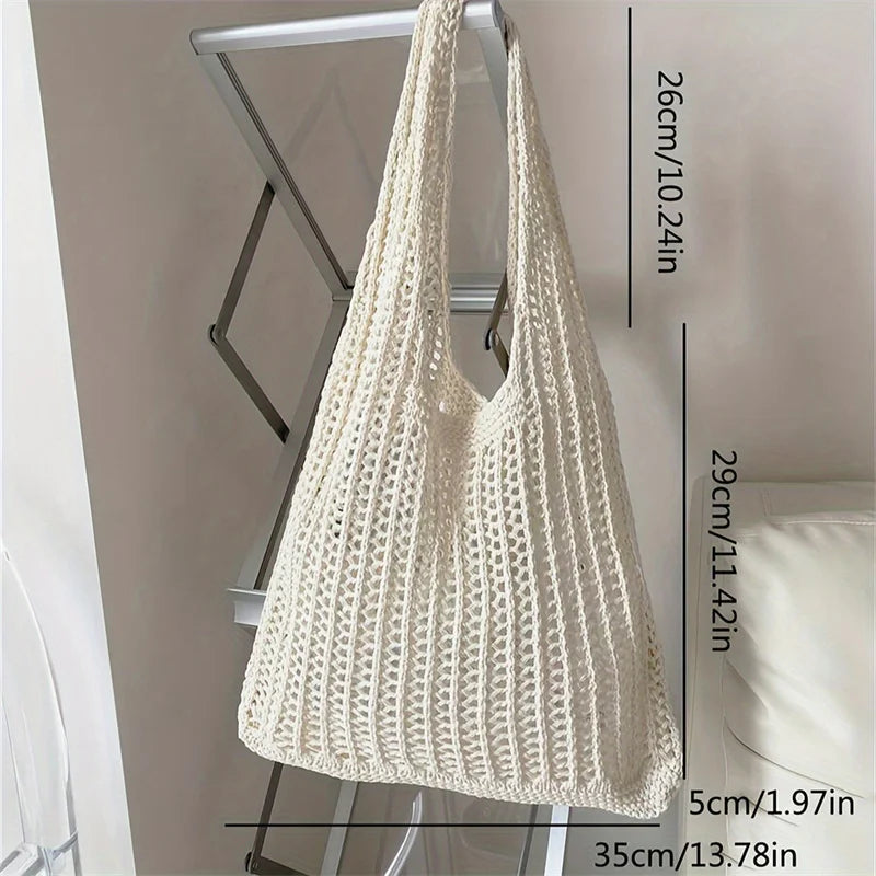 A cream-colored bohemian knit shoulder bag hanging against a white wall with size measurements.