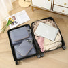 A black travel packing cube set containing a laptop, clothing, and additional fabric cubes on a wooden floor.