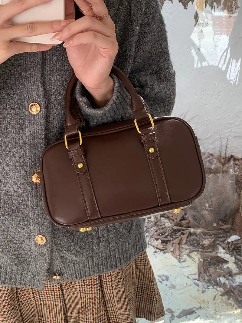 A brown vintage PU leather shoulder bag carried by a person wearing a gray sweater and plaid skirt.