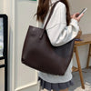 A woman holds a dark brown leather tote bag against a light background.