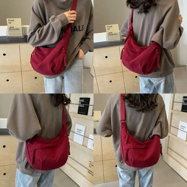 A person is holding a maroon canvas crossbody shoulder bag against a light background.