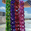 A hand holds a necklace featuring chunky gold acrylic Cuban links in various vibrant colors like green, purple, pink, and red