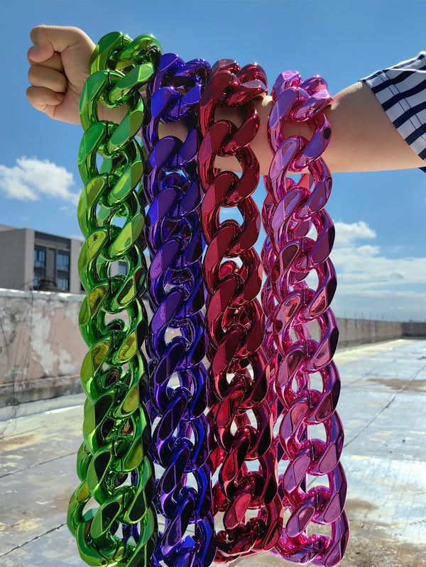 Una mano sostiene un collar con eslabones cubanos de acrílico dorado grueso en colores vibrantes como verde, púrpura, rosa y 