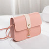 A light pink fashion square crossbody bag with a beige strap and gold chain charm resting on a white surface.