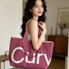 A woman holds a pink knitted large tote bag with a white logo against a light background.