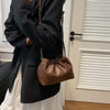 A woman wearing a black blazer and white skirt holds a brown PU leather chain shoulder bag.