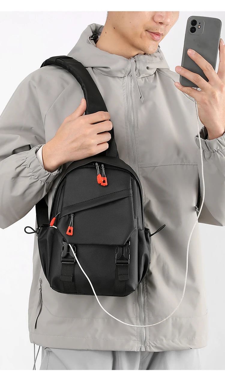 Un homme en veste grise tient un sac de sport noir avec des accents orange.