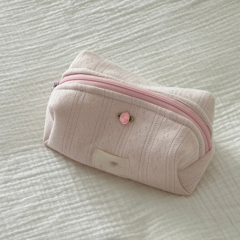A light pink striped cotton toiletry pouch with a zipper and a small rose detail lying on a white surface.