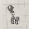 Silver stainless steel alphabet letter charm with a lobster clasp placed on a grid ruler.