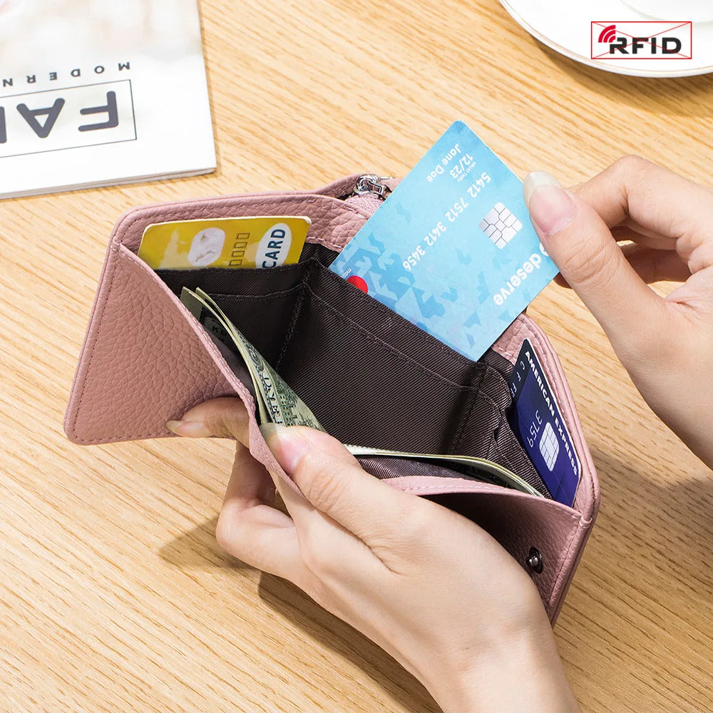 Una mano abre una cartera con cremallera de cuero rosa para mostrar una tarjeta de crédito y una tarjeta bloqueadora de RFID.