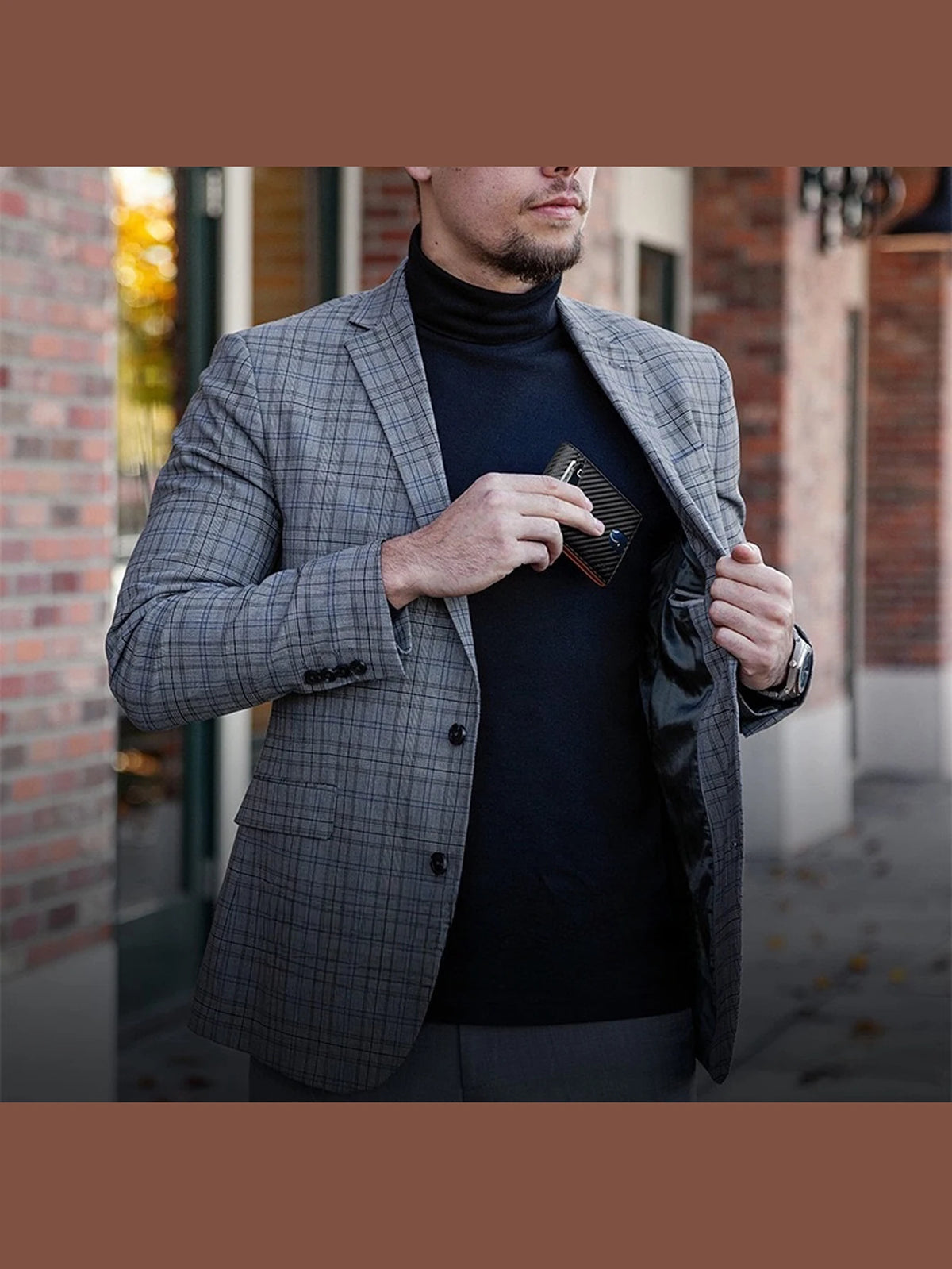 A man wearing a gray plaid blazer and black turtleneck holds a carbon fiber microfiber wallet.